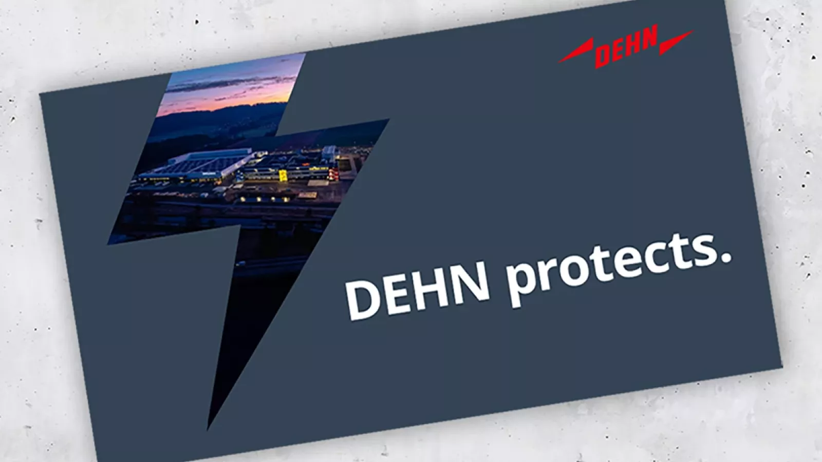 Dark blue rectangular card with a lightning bolt shape cutout showing a building with solar panels at sunset and the text 'DEHN protects.' in white with a red DEHN logo.