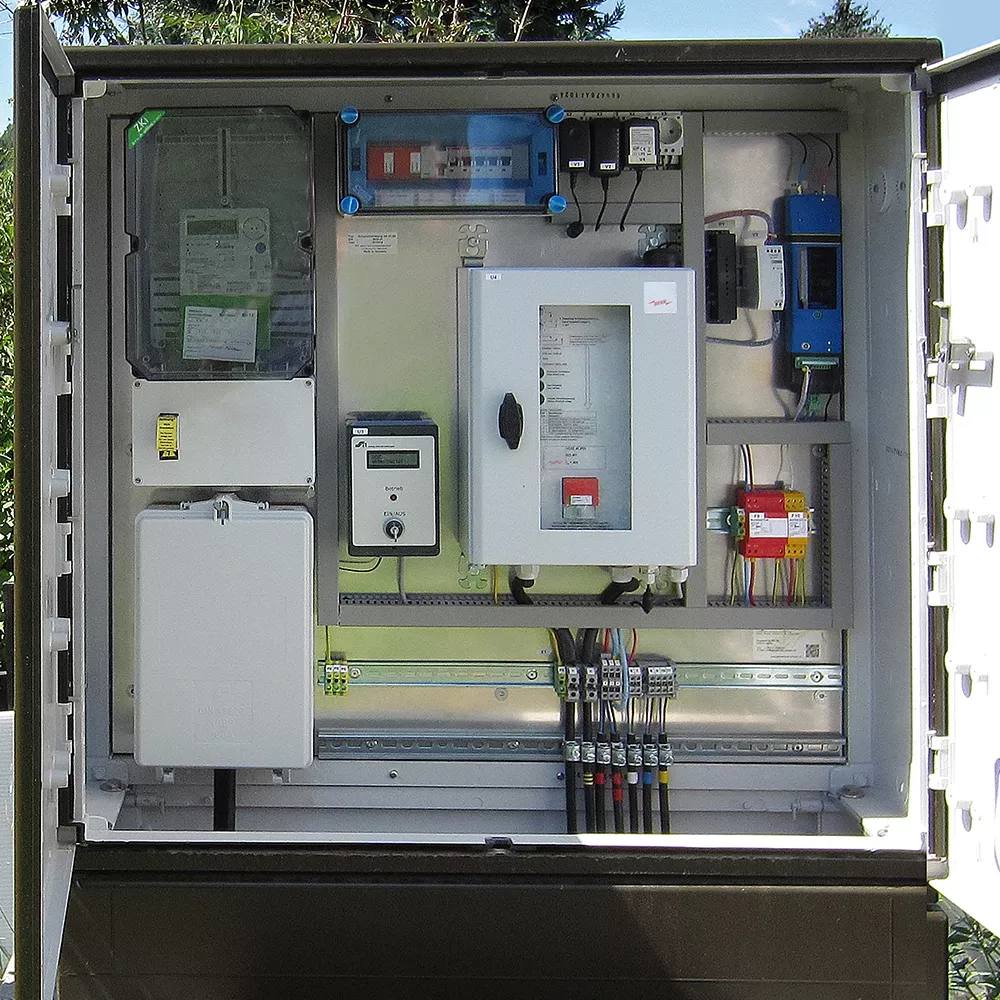 Open outdoor electrical cabinet showing meters, control units, wiring terminals, and surge protection components mounted on a panel.