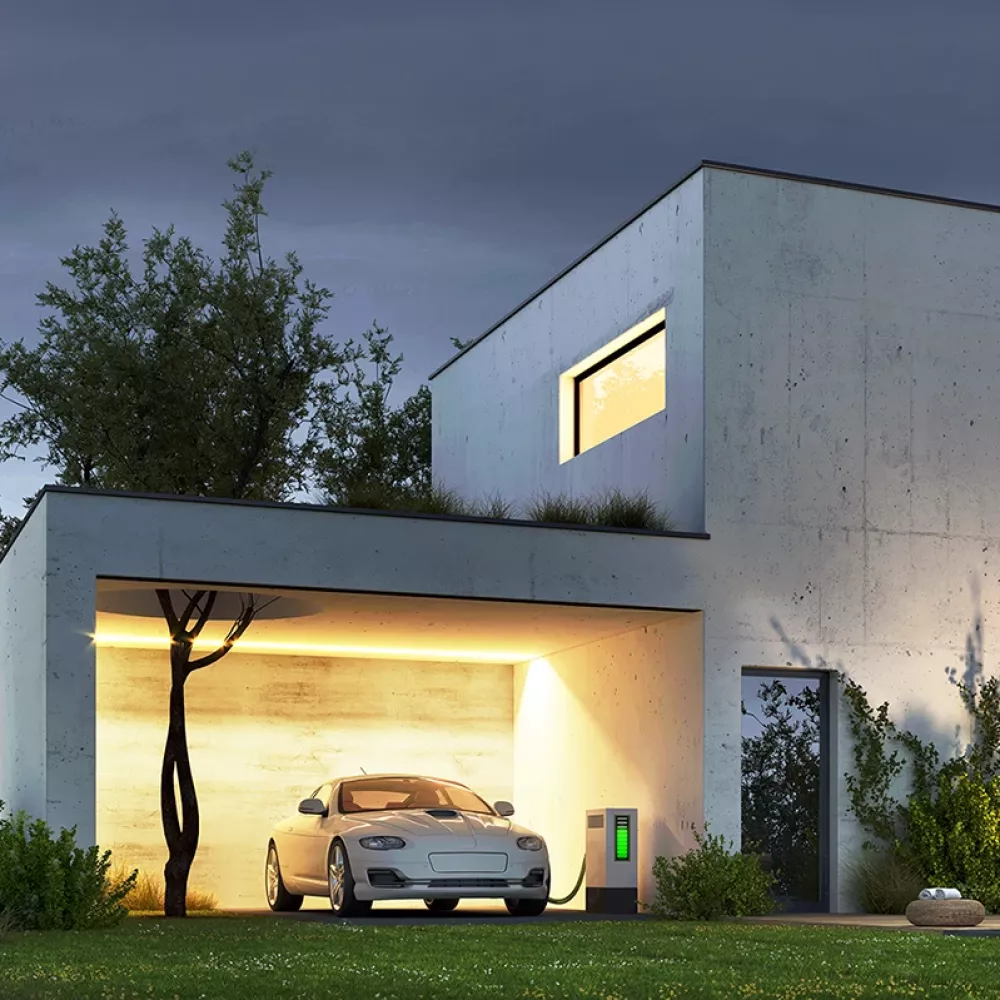 Modern concrete house at dusk with illuminated windows, an electric car charging in the garage, garden lighting, and a pool in the foreground.