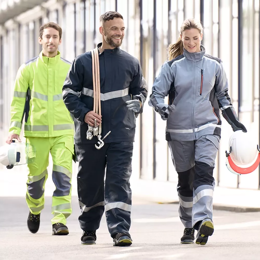 Three technicians in protective workwear walking through an industrial facility, carrying helmets and safety equipment.