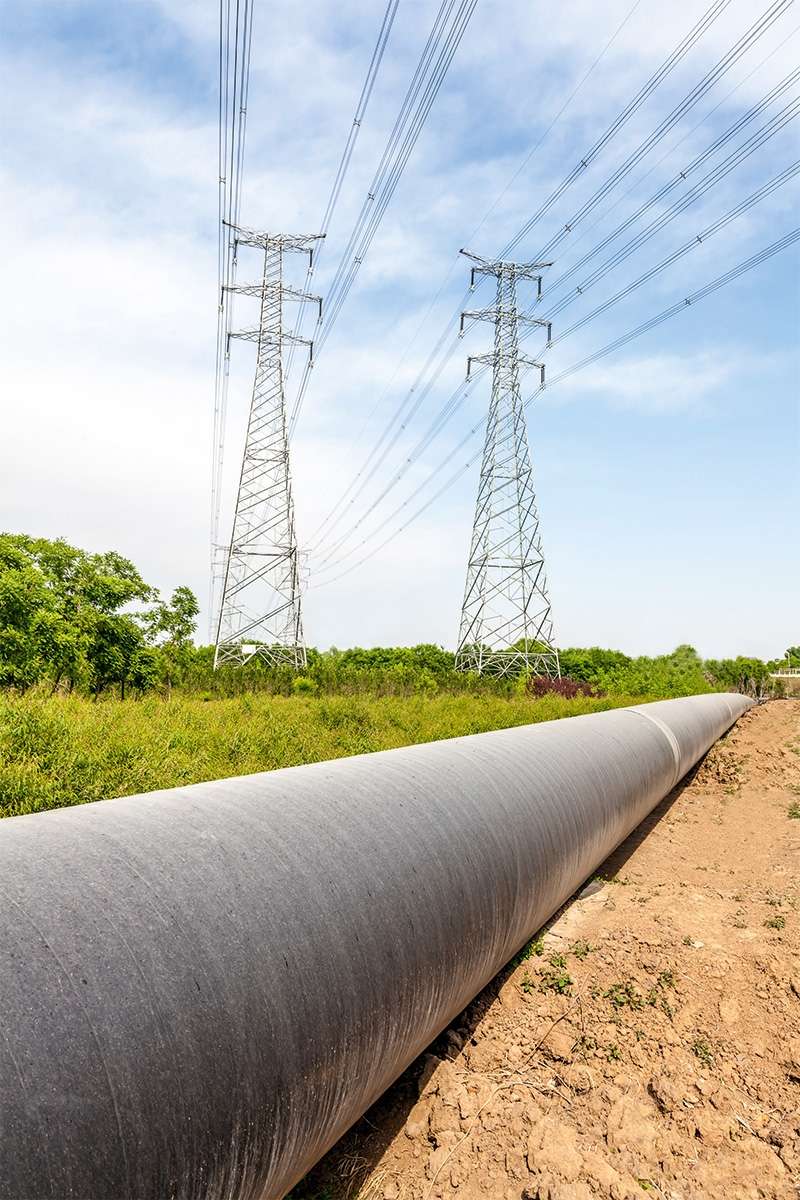 Hochspannungsleitung und Pipeline auf grüner Wiese vor Wald.
