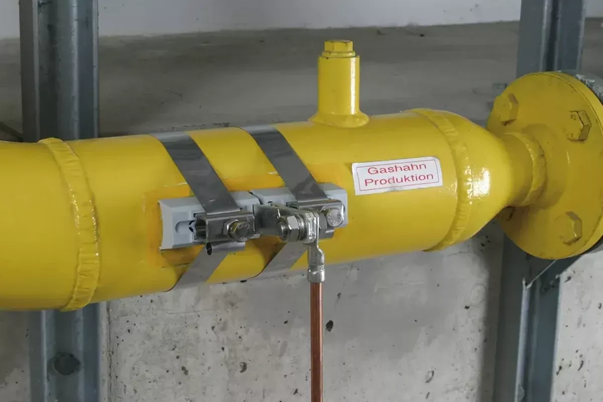 Zwei an einer gelben Gasleitung montierten Bandrohrschellen. 