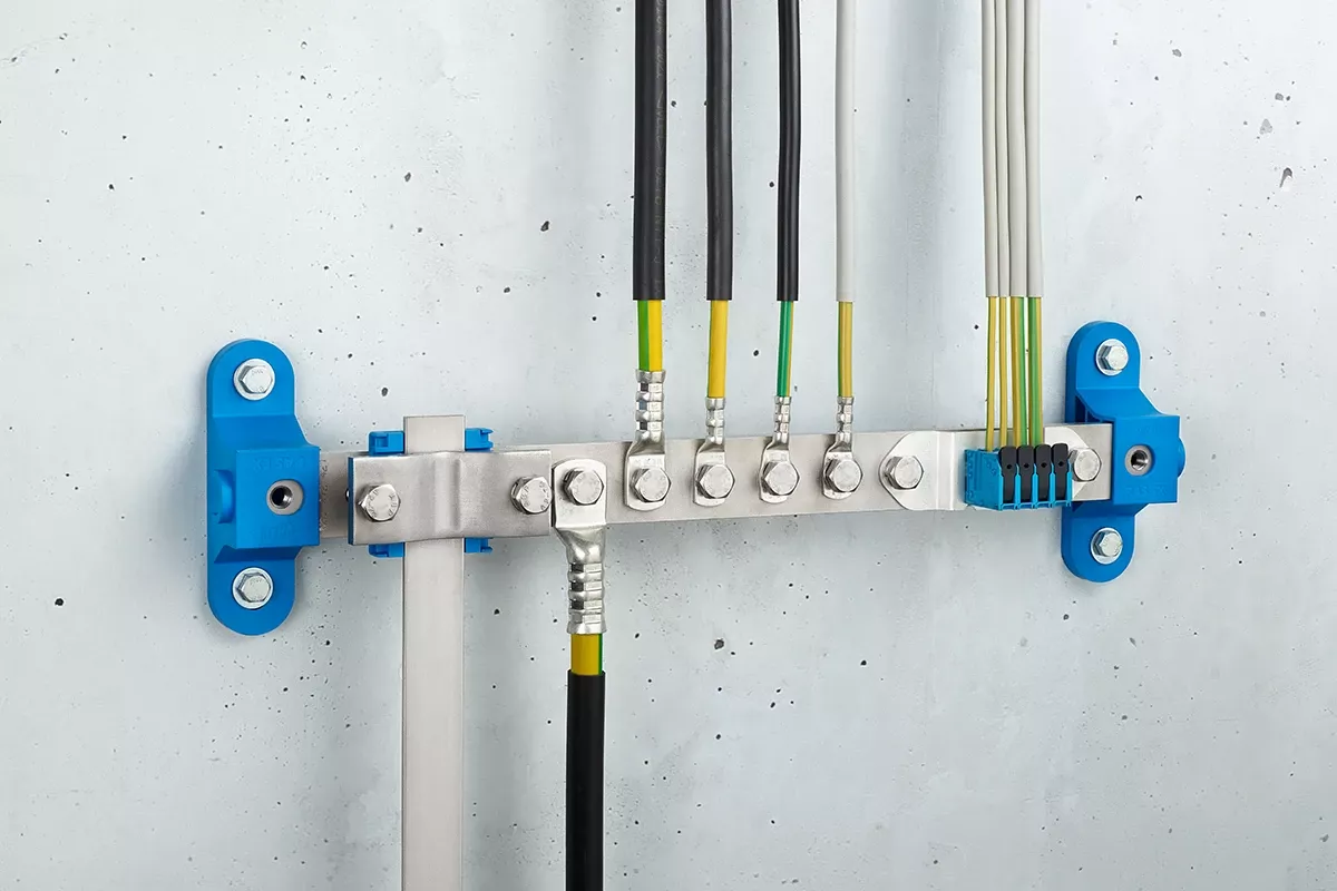 Potentialausgleichsschiene mit blauen Wandanschlüssen und schwarzen Kabeln, montiert an grauer Betonwand. 