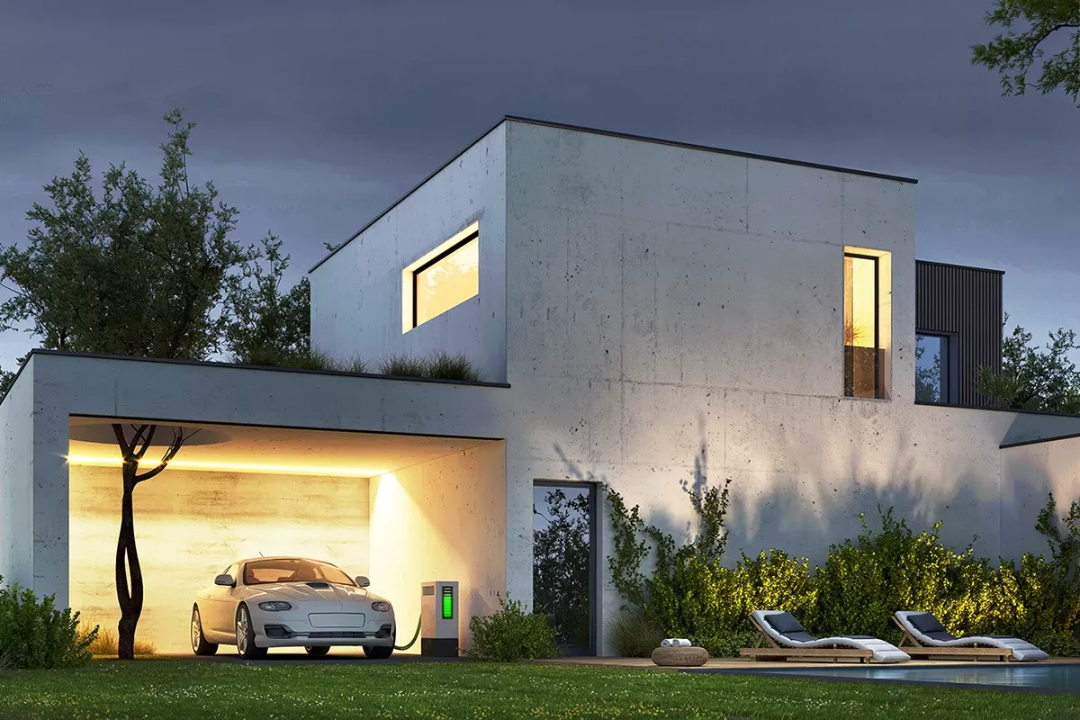 Modern concrete house at dusk with illuminated windows, an electric car charging in the garage, garden lighting, and a pool in the foreground.
