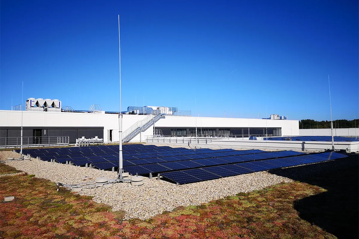 Rooftop solar panels installed on industrial building with lightning protection masts under clear blue sky.