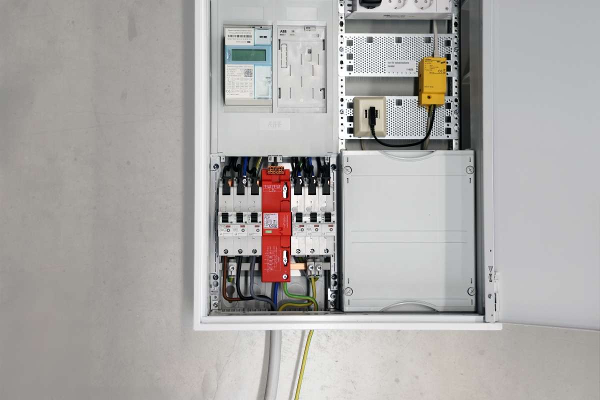 Geöffneter Stromverteiler mit Sicherungen, Zähler und rotem Überspannungsschutzmodul, sauber verdrahtet in weißem Schaltschrank